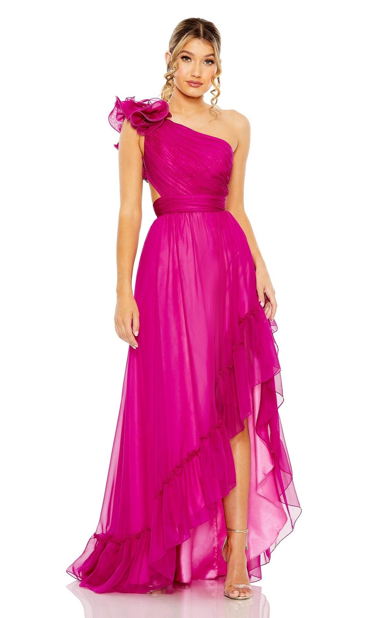 A woman models the Mac Duggal Long Formal Dress 67989 in bright pink, featuring a one-shoulder design with floral detail and a ruffled hem, standing against a plain white background.